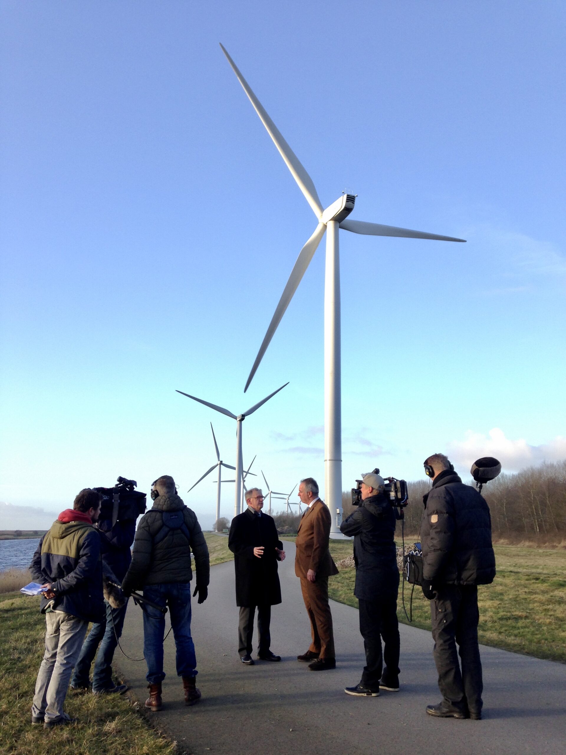 Een futuristisch landschap met golvende velden vol zonnepanelen, windturbines en snelwegen met rijdende auto's, met in de verte een moderne stad onder een zonsondergang. (AI-gegenereerd)